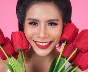 Uśmiechnięta piękna kobieta, trzymająca bukiet czerwonych kwiatów blisko twarzy.